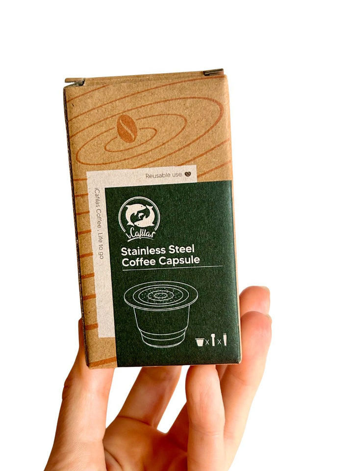 Hand holding a  stainless steel reusable nespresso capsule package against a white background